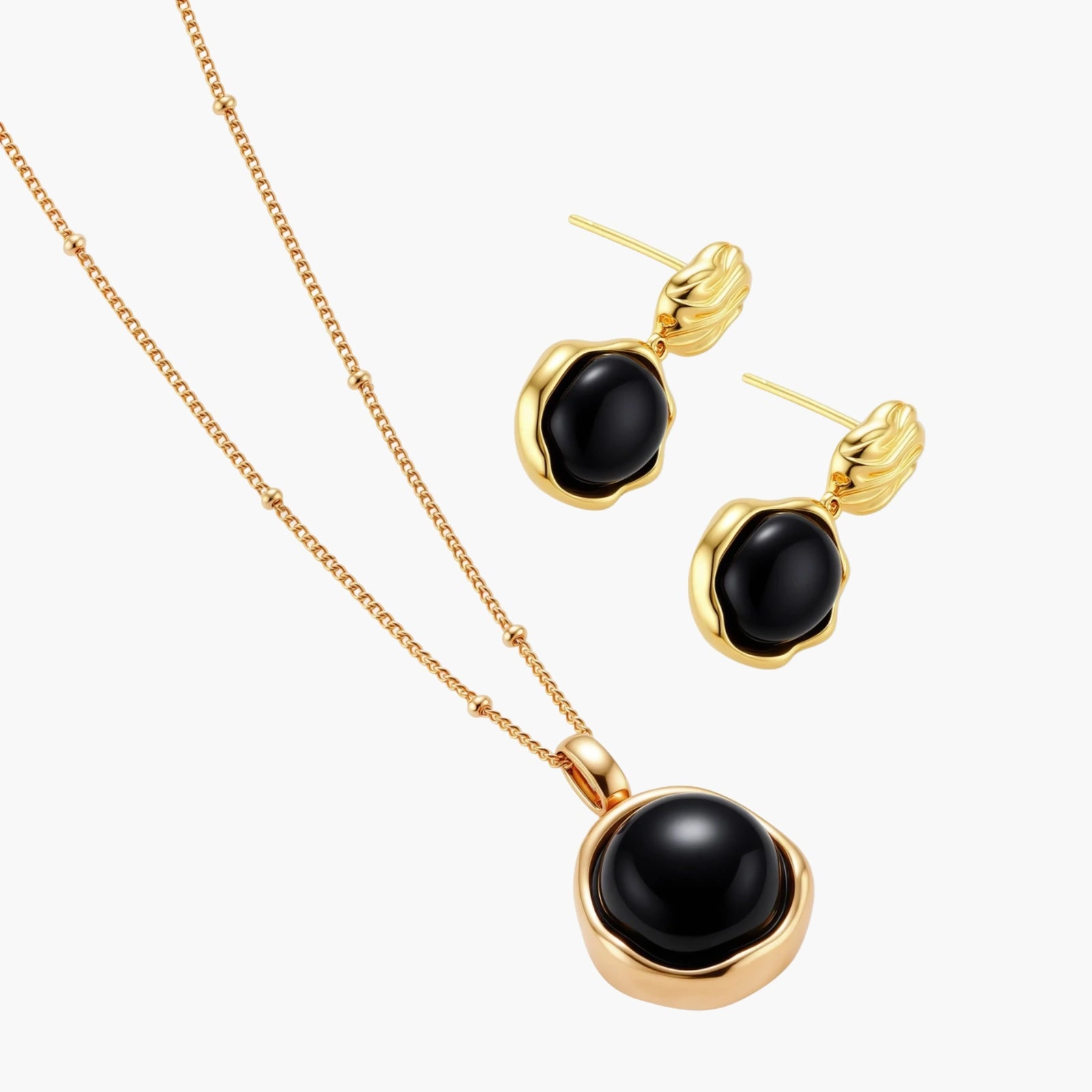 Circular black agate pendant on gold-plated sterling silver chain against cream background, showing modern minimalist design.